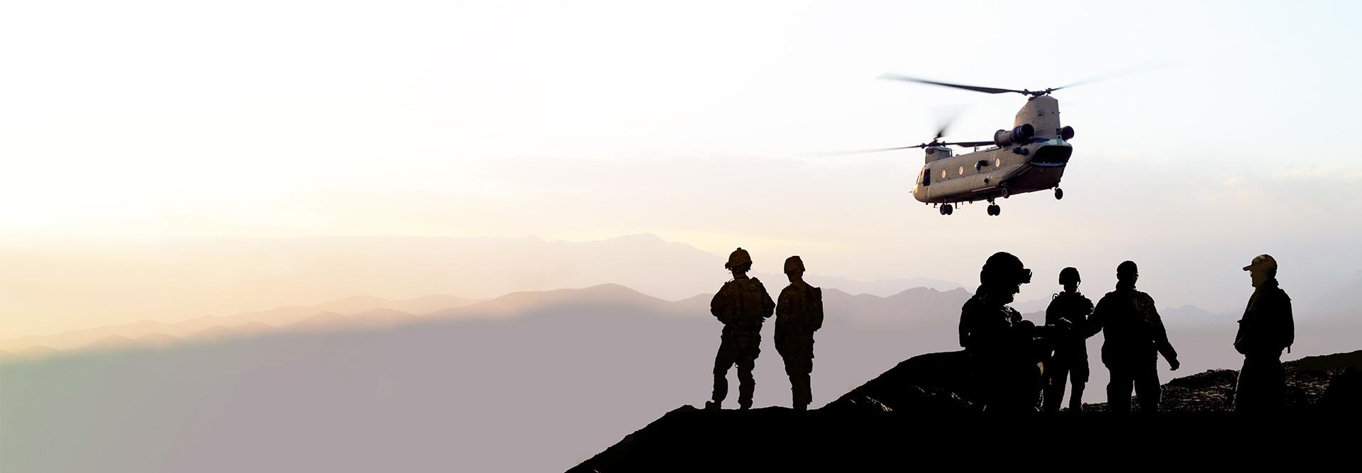 Soldiers standing on a hill, military helicopter flying at sunset