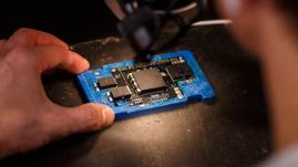Technician examining a semiconductor chip on a PCB using a microscope.