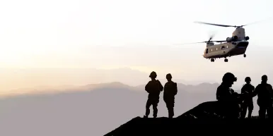 Soldiers standing on a hill, military helicopter flying at sunset